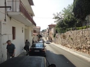 Street with stone wall on the sunny side, white buildings and pedestrians on the shady side